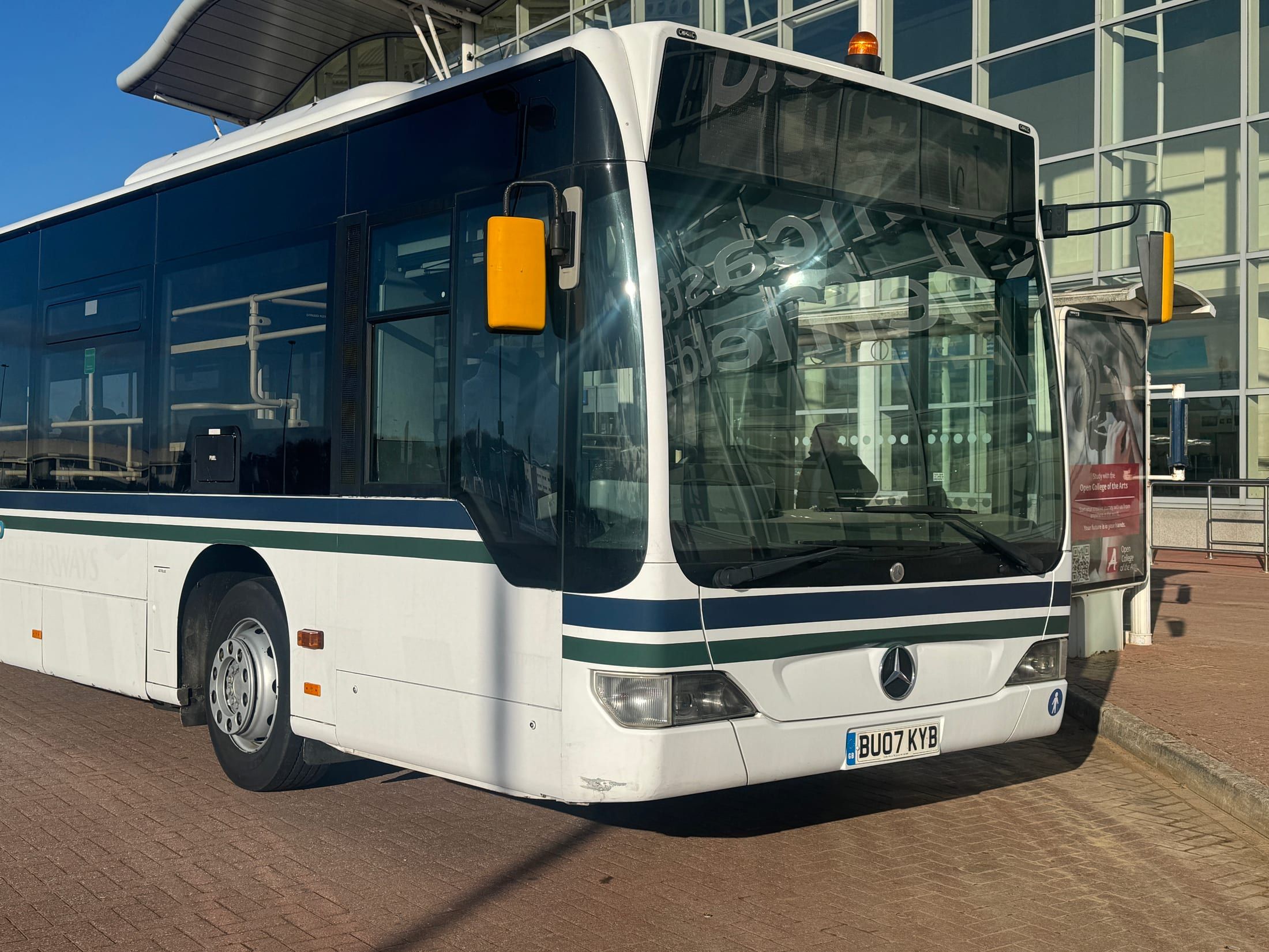 White and dark blue liveried coach with tinted windows, parked outside a glass-fronted terminal building.